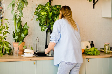 Young woman washing dishes at home in kitchen. Household and home hygiene routine.