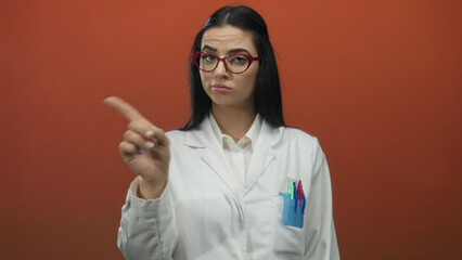 Woman in white uniform with red glasses gesturing no with finger in front of red wall expressing...