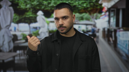 Man shows bare thumb up gesture on building terrace overlooking blurred tables and umbrellas; optimism.