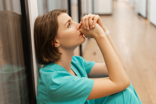 Exhausted doctor sitting on floor in hospital corridor is praying