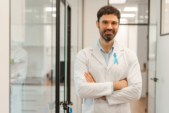 Smiling bearded doctor wearing blue ribbon showing support for prostate cancer awareness month