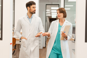 Fototapeta premium Doctors wearing lab coats are walking and discussing in hospital corridor