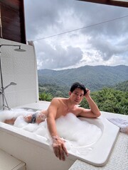 Handsome Man Relaxing in a Bubble Bath with Stunning Mountain View Amid Gentle Rain