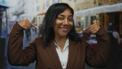 Woman in brown suit jacket and white shirt points finger to self on busy city street; confidence...