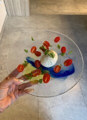 Closeup image of a caprese salad on a glass plate being held by a woman’s hand