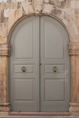 Old grey wooden double door with arched entry and massive ring handles, entrance to a historic building