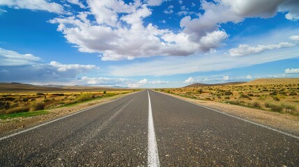 Fototapeta premium Highway Horizons: Dynamic Picture of Asphalt Highway – Smooth Black Pavement Cutting Through Green Fields and Distant Hills, Yellow Center Lines, Roadside Guardrails, and Trucks Speeding Under a Cloud