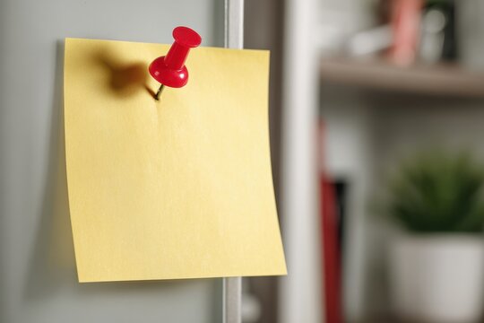 Yellow sticky note with red pushpin for effective reminders or messages on a clear surface for home and office organization needs