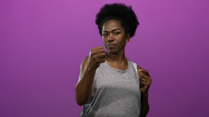 African american woman boxing against an isolated purple background, showcasing energy and fitness through focused expressions and dynamic movements.