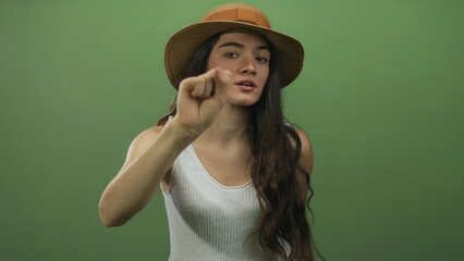 Young hispanic woman softly knocking with bare hand on camera glass in green studio while leaning...