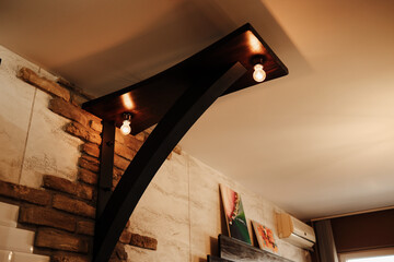 Modern wooden ceiling fixture with bulbs, mounted on a stone wall inside a stylish interior....