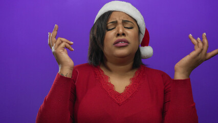 Woman in festive santa hat and red sweater expresses frustration against a vibrant purple backdrop,...