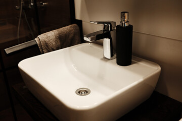 Close-up of modern sink faucet and black soap dispenser in a minimalist bathroom setting. Bathroom interior details in a modern apartment or hotel.