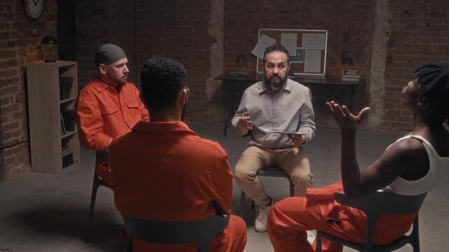 Medium full shot of middle-aged Caucasian male prison counselor teaching anger release techniques to multinational convicts with focus on deep breathing, while conducting rehabilitation course