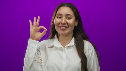 Woman with long brown hair in white shirt showing ok sign with her bare right hand in purple...