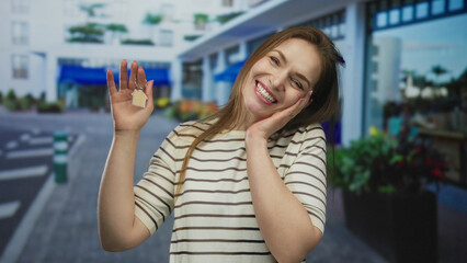 Young caucasian woman holding house keychain in hand on a blue street outside shops; new home...