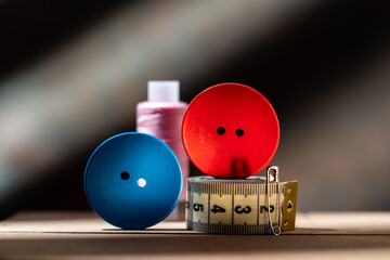 Red and blue buttons with threads and measuring tape for sewing.