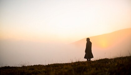 Fototapeta premium A silhouette of a person stands against a bright orange and pink sunset background.