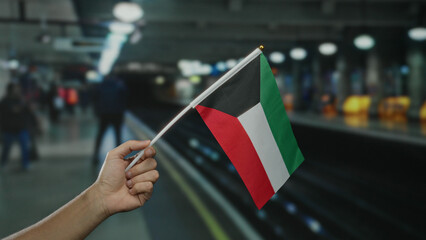 Man holding kuwaiti flag at indoor train station, capturing diverse commuter environment with...