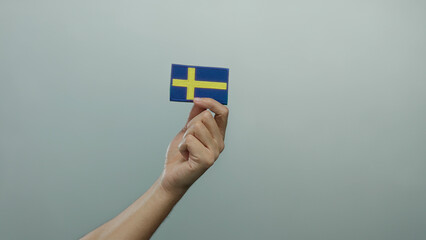 Caucasian man hand holding swedish flag embroidery against isolated white wall background.