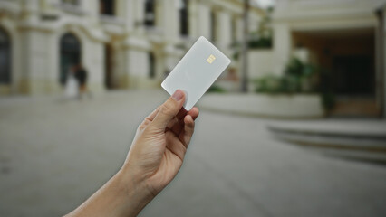 Man holding white card in urban street setting showcases a modern male interaction with financial technology outdoors in a city environment.