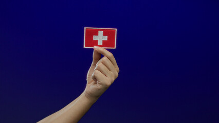 Man holding a swiss flag embroidery patch against a blue isolated background, capturing a symbolic...