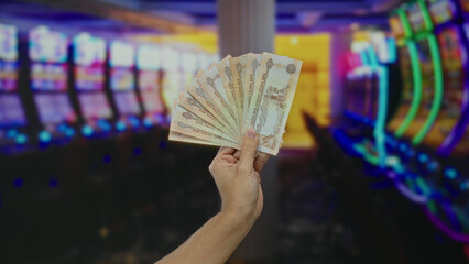 Man holding united arab emirates dirham banknotes indoors at a casino with slot machines in the...