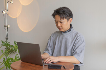 Focused Asian man working on laptop in a modern home office. Freelancer concentrating on a project,...