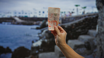 Hand holding singaporean banknote by the seaside captures a tranquil vacation moment, highlighting...