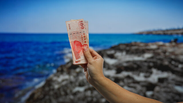 Hand holding taiwan banknote near seaside city suggesting business and investment opportunities outdoors by the beach. - Powered by Adobe