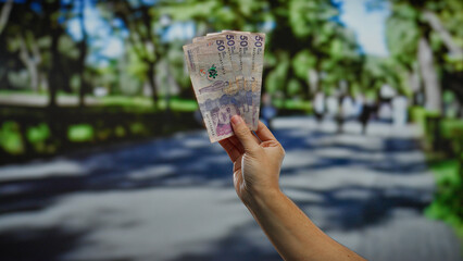 Hand holding colombian pesos in an outdoor city park, emphasizing business and finance in an urban...