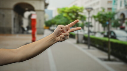 Man hand showing peace gesture on a city street with blurred urban background depicting outdoor environment.