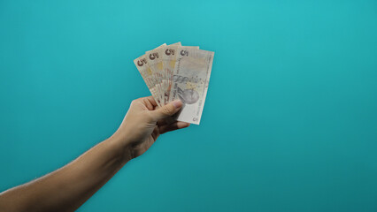 Man holding turkish lira banknotes against an isolated blue background, emphasizing finance and...