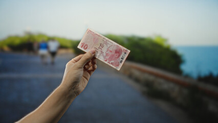 Man holding turkish lira banknote on city street with blurred background, capturing urban outdoor...