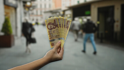 Man holding hungarian forint banknotes on a bustling city street, exemplifying an outdoor financial...