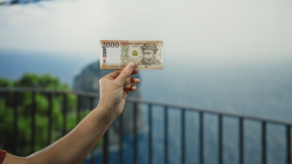 Man holding hungarian forint banknote at seaside, with ocean view in background, showcasing...