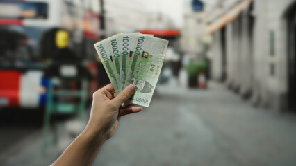Man holding south korean won banknotes at an outdoor bus stop, capturing a casual city moment with...
