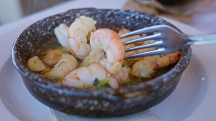 Closeup of sizzling shrimp in garlic oil at a mediterranean restaurant table indoors.