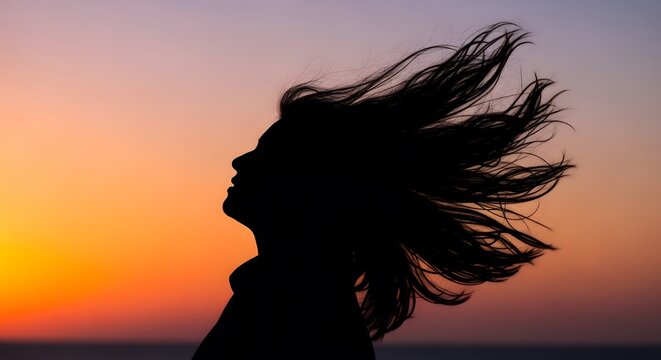 Silhouette of a woman with hair blowing in the wind against a vibrant sunset sky, symbolizing freedom and new beginnings.
