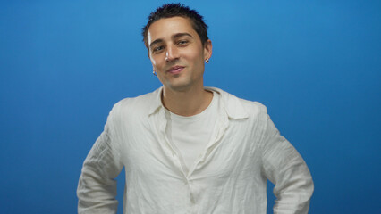 Young man with a white shirt stands confidently against a vibrant blue wall, showcasing a relaxed...