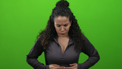 Hispanic woman experiencing stomach pain against a bright green background, highlighting the...