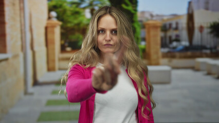 Woman puts up her finger as a refusal on the street where a young blonde stands outdoors making a...