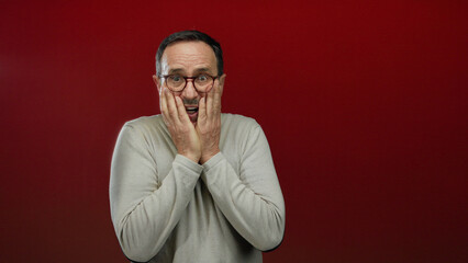 Mature hispanic man with glasses looking worried against a bold red background