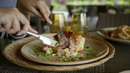 Woman enjoying seafood dish with hands at a restaurant table, showing a vibrant and fresh meal presentation with cutlery and modern dining setup.