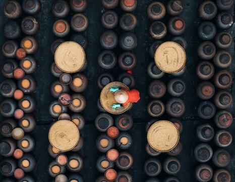 Aerial view of a person wearing a hat and red shirt standing between rows of soy sauce jars, Soy sauce maker, Ban Yen Nhan village, Hanoi Vietnam.