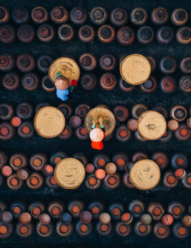 Aerial view of conical hats arranged in neat rows, interspersed with circular trays, creating a textured tableau of warm browns and earthy tones, Soy sauce maker, Ban Yen Nhan village, Hanoi Vietnam.