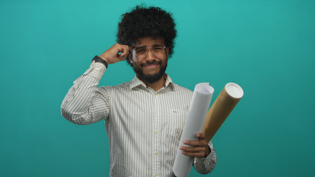 African american man holding blueprints gesturing confusion against green wall background.