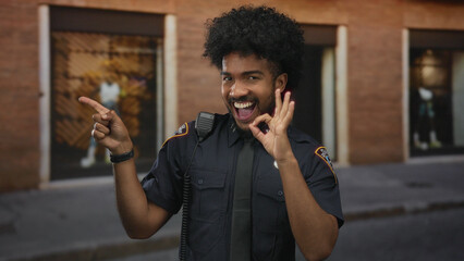 Smiling african american police officer in uniform making an ok gesture on a city street suggesting confidence and friendliness in a busy outdoor urban environment.