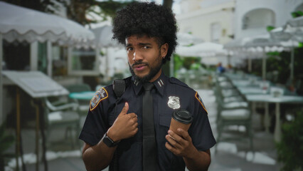 Police officer in uniform gestures while holding coffee on an outdoor restaurant terrace conveying...