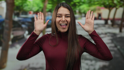 Woman smiling outdoors on a sunny day with a joyful expression on an urban street lined with green...